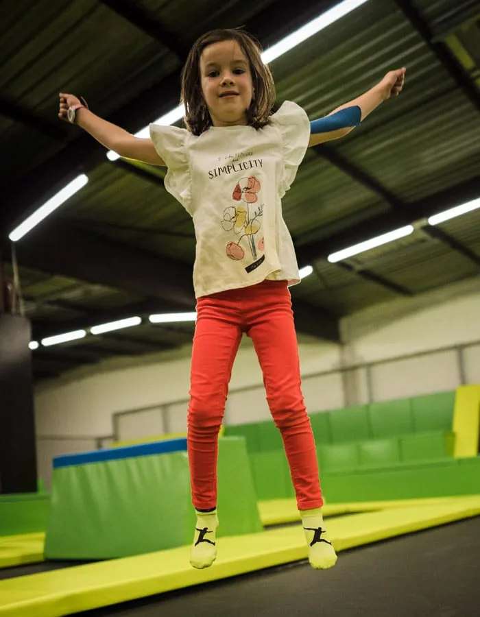 Fillette en plein saut, bras écartés, sur les trampolines du parc