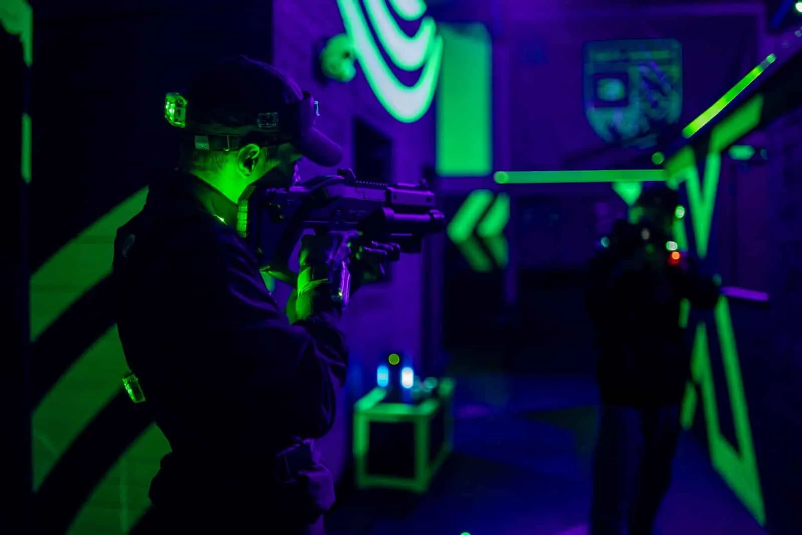 Joueur en joue dans le labyrinthe du Laser Game, sous les néons verts et violets