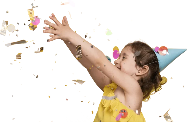 Petite fille coiffée d’un chapeau de fête, lançant une poignée de confettis en l’air