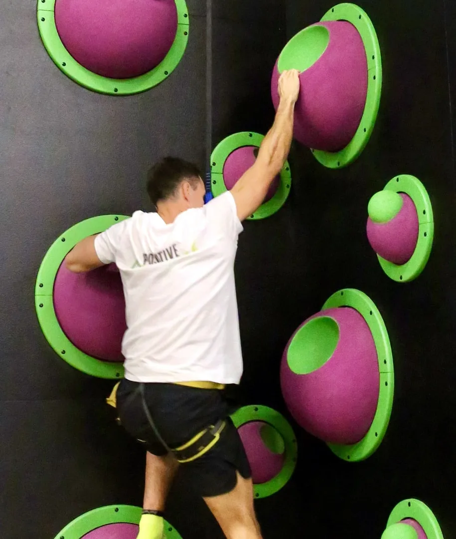 Grimpeur en équilibre sur les coupoles vertes et violettes du mur du Fun Wall