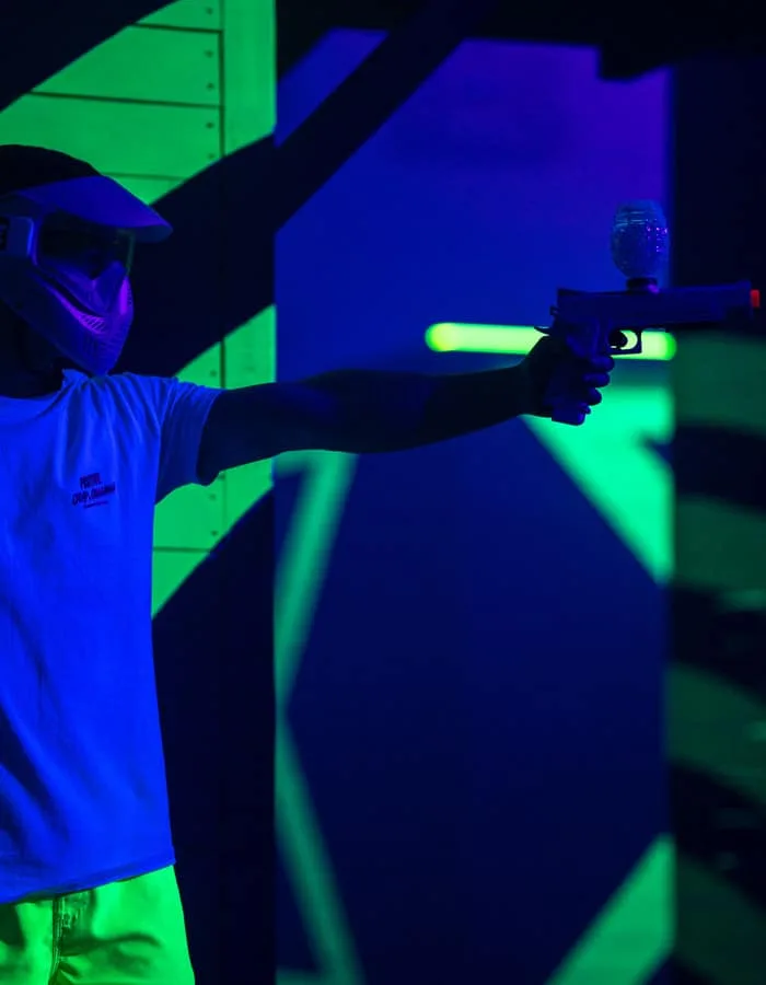 Joueur masqué visant au blaster dans un couloir en lumière noire